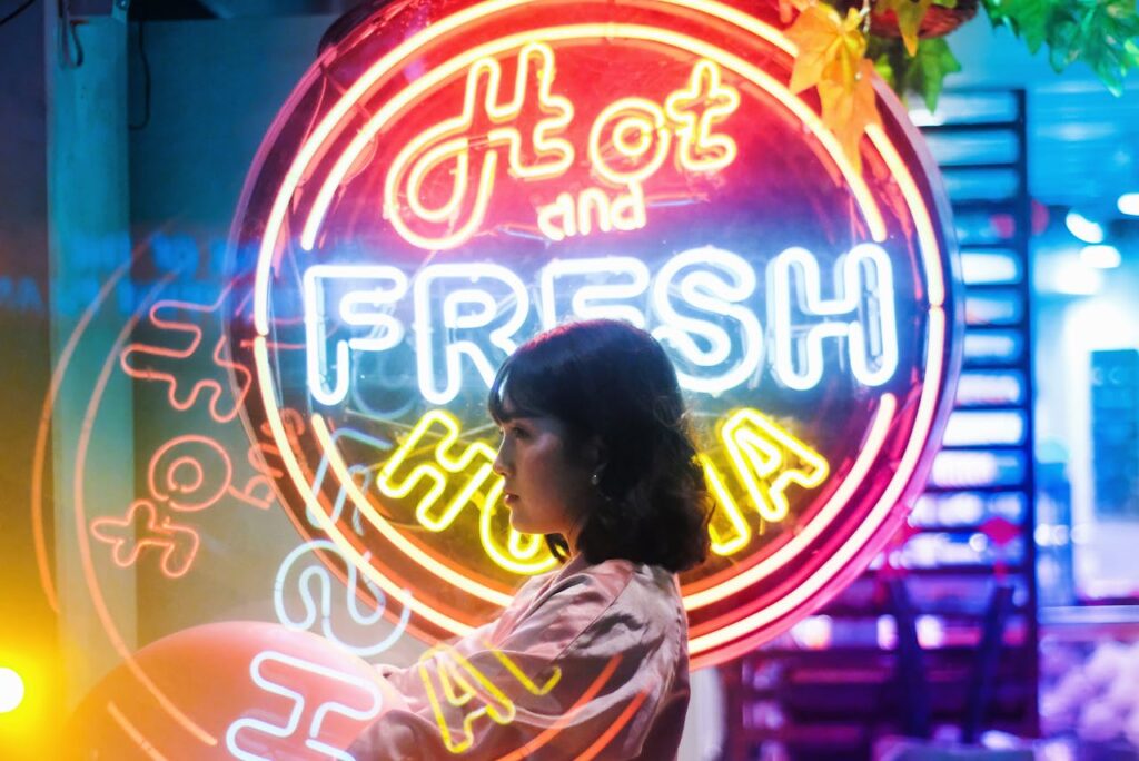 Leuchtbuchstaben Shop Neonreklame Bild Ein fesselndes Seitenprofil einer Frau vor einem hellen Neonschild mit der Aufschrift „Hot and Fresh“, das eine surreale Atmosphäre schafft.